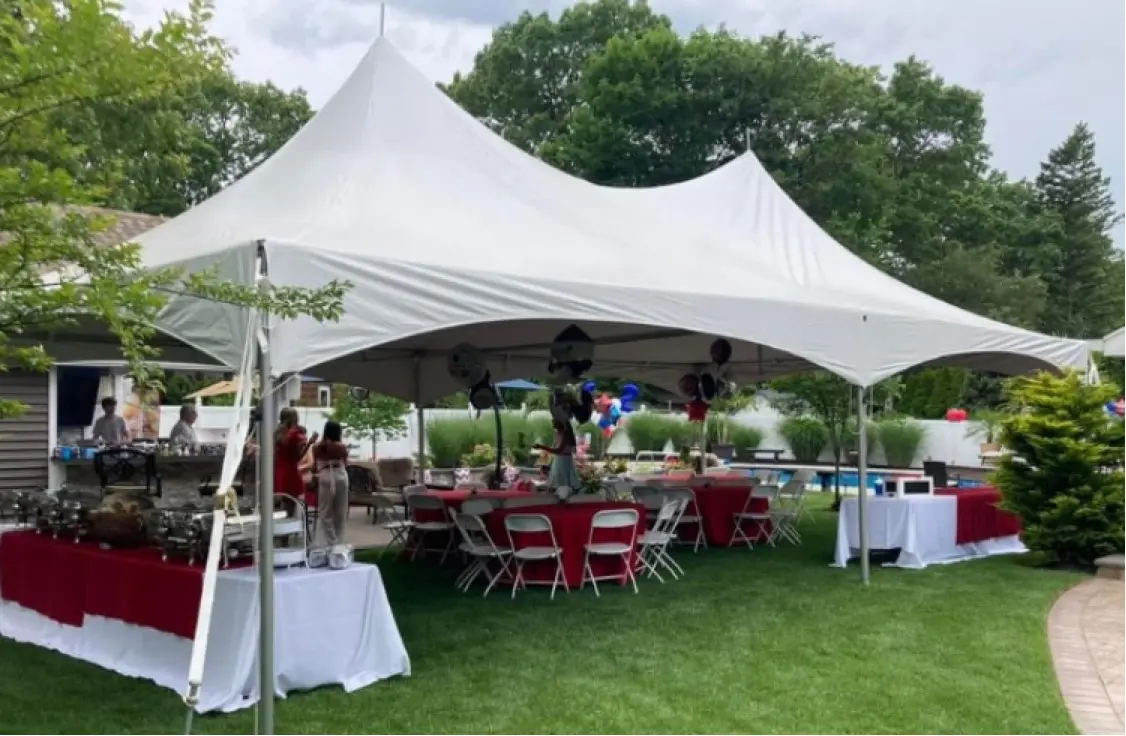 A tent with tables and chairs in the grass.